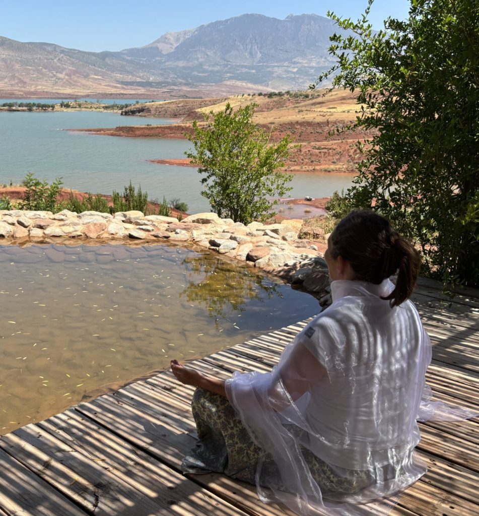 Femme méditant au bord d'un lac au Maroc, illustrant la retraite de Danse de l'Être® "Danse-Terre-Happy, la médecine des éléments"